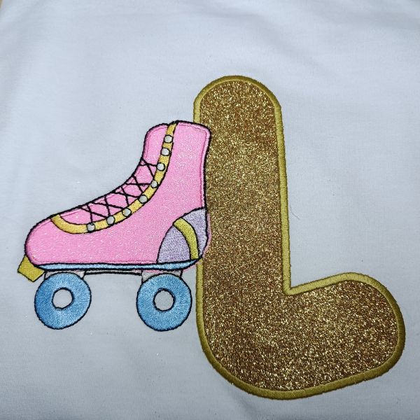 Pormenor da t-shirt criança branca com aplicação de vinil têxtil e bordado em inicial L e patim.