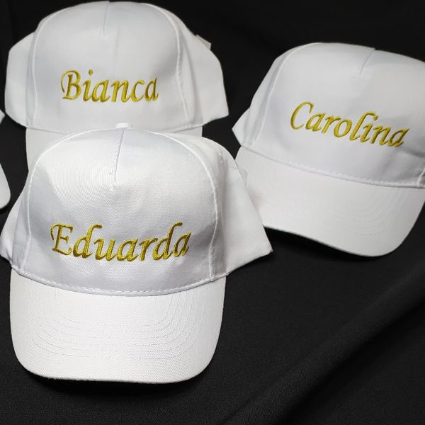 Bonés brancos com nomes bordados a dourado.