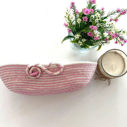 Cesta oval em cordão de algodão cru e barbante rosa na parte exterior.
