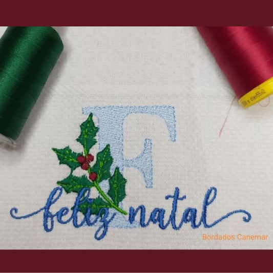 Pano de cozinha com Feliz Natal e um ramo de azevinho bordados.