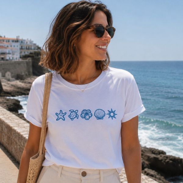 Mulher a usar t-shirt branca com cinco ícones marinhos bordados: estrela-do-mar, tartaruga, flor de hibisco, concha e sol.