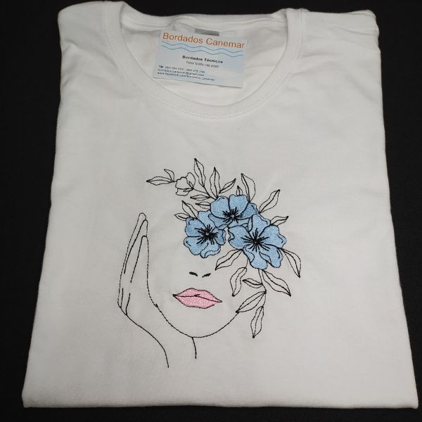 T-shirt branca com rosto bordado e flores azuis.