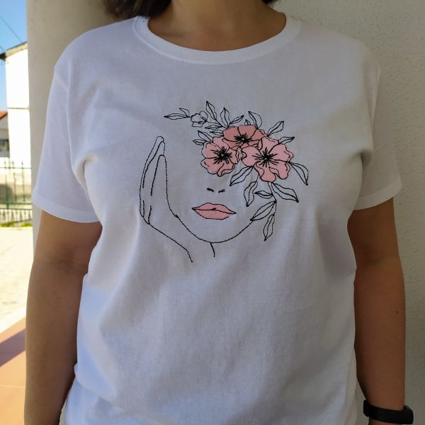 T-shirt branca com rosto bordado e flores rosa.