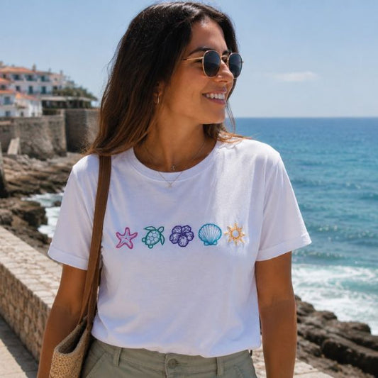 Mulher a usar t-shirt branca com cinco ícones marinhos bordados: estrela-do-mar, tartaruga, flor de hibisco, concha e sol.